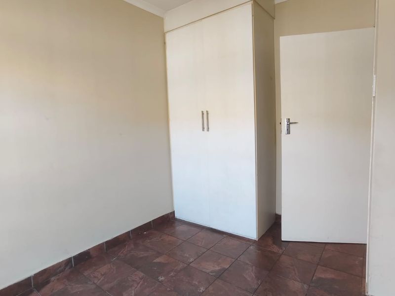 A vacant bedroom featuring tiled flooring, a built-in wardrobe, and neutral wall finishes.