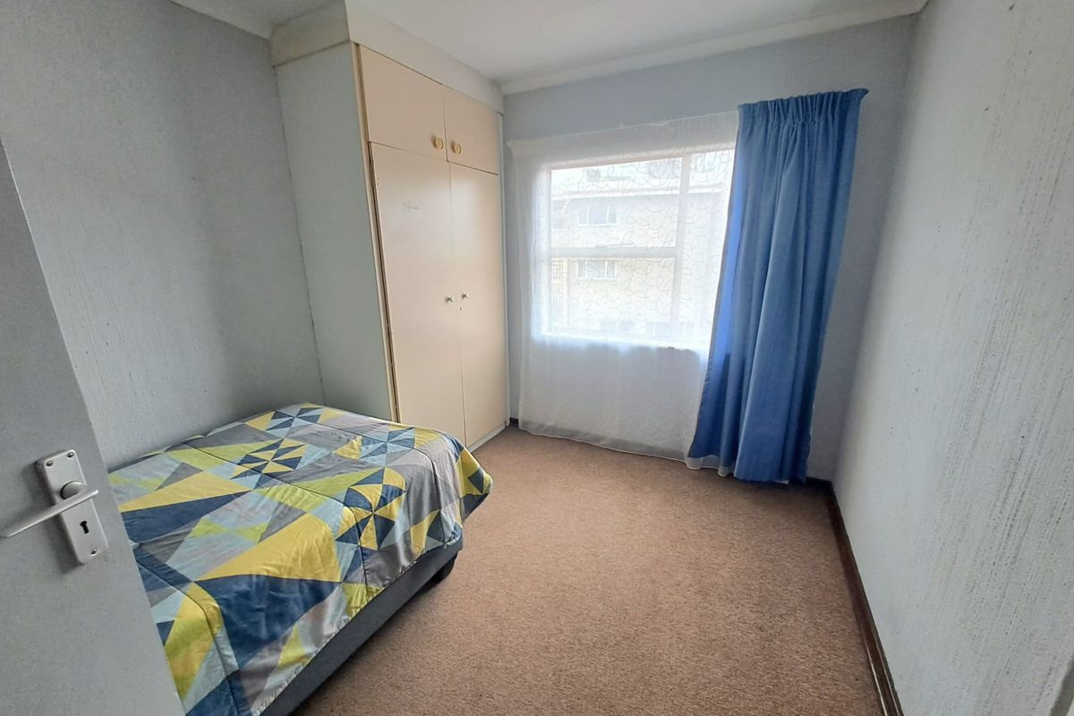 A functional bedroom featuring neutral walls, carpet flooring, and a built-in wardrobe, offering a practical space with potential for modernization.