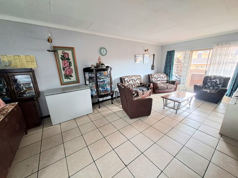 A spacious living room featuring neutral ceramic floor tiles and a large sliding glass door providing natural light and access to the exterior.