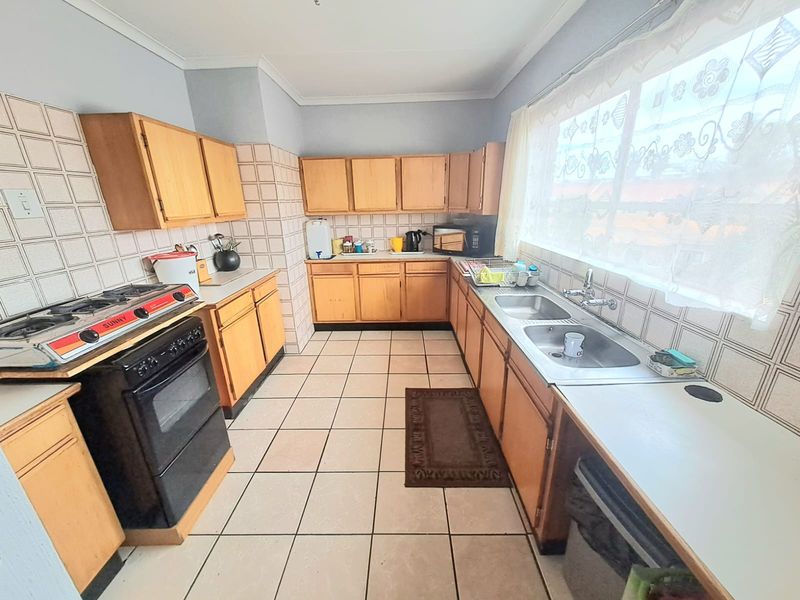 A functional kitchen featuring wooden cabinetry, tiled splashbacks, a double basin sink, and ceramic floor tiles, offering a classic layout with ample storage space.