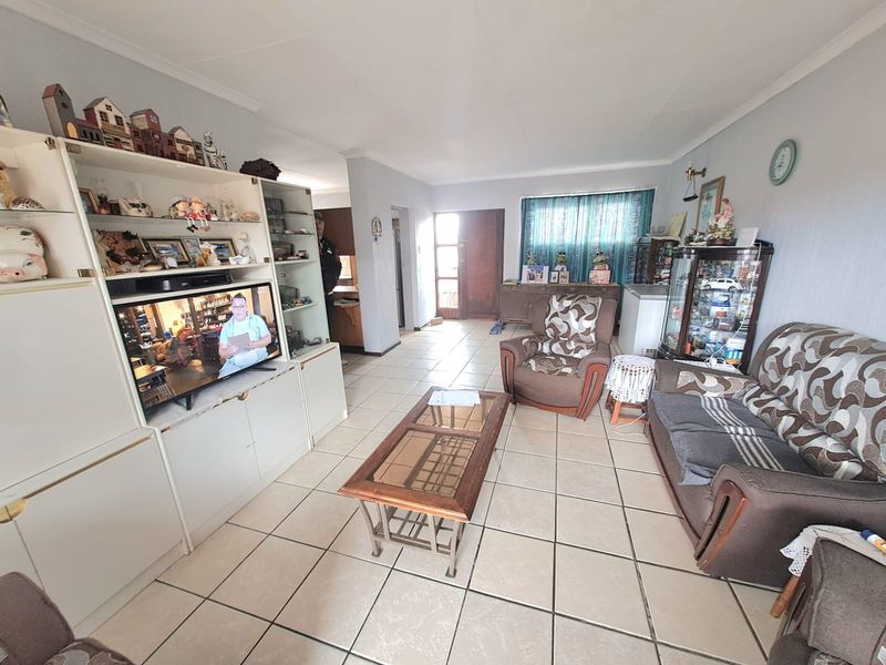 A spacious living room featuring neutral tiled flooring and a built-in display shelving unit, offering a functional layout with direct access to the entrance.