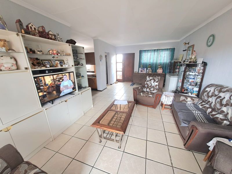 A spacious living room featuring ceramic floor tiles, coved ceilings, and built-in display cabinetry, offering a functional layout with direct access to the entrance.