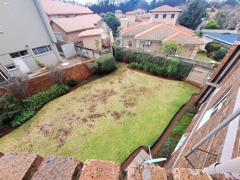 An elevated view of a private rear garden featuring a lawn area, brick boundary walls, and established perimeter landscaping within a residential complex.