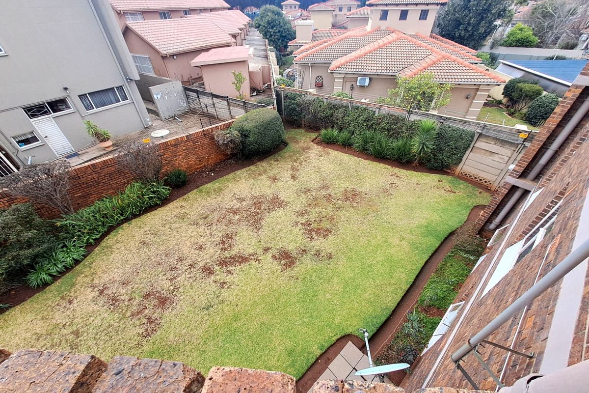 An elevated view of a private rear garden featuring a lawn area, brick boundary walls, and established perimeter landscaping within a residential complex.