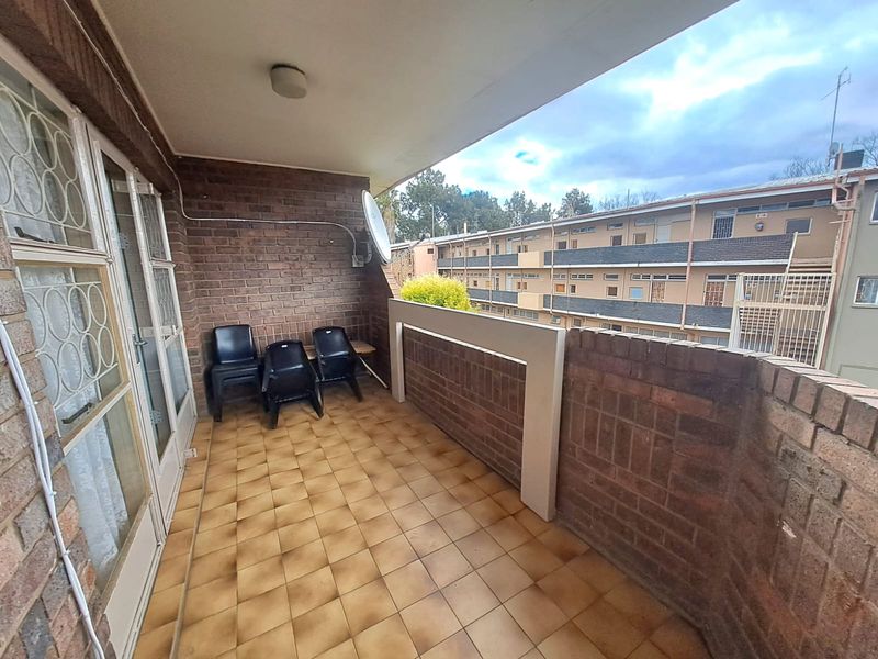 A covered balcony featuring brick walls and tiled flooring, offering an outdoor space with views of the surrounding apartment complex.