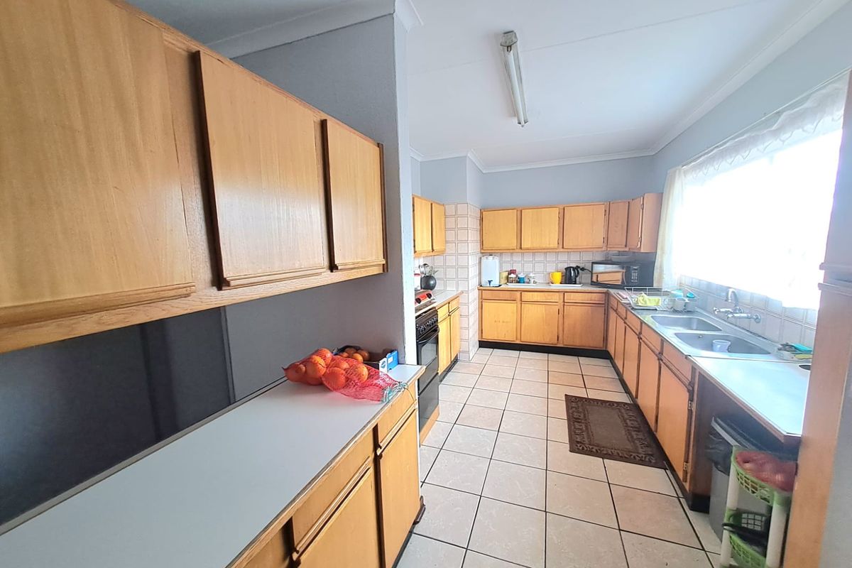 A functional kitchen featuring wooden cabinetry, laminate countertops, a double bowl stainless steel sink, and ceramic tile flooring.
