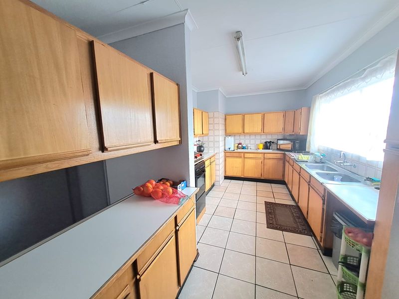 A functional kitchen featuring wooden cabinetry, laminate countertops, a double bowl stainless steel sink, and ceramic tile flooring.