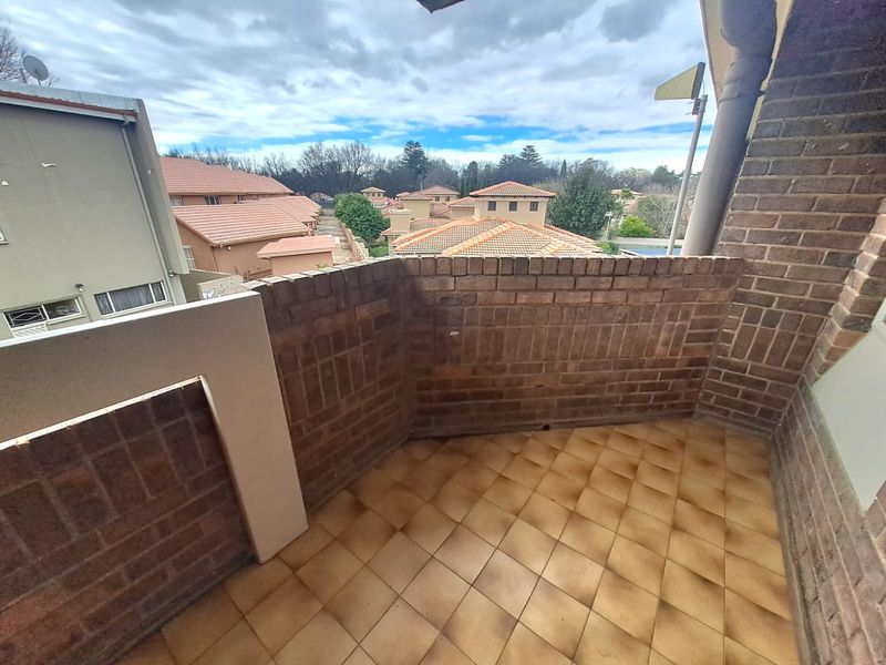 An open balcony featuring brick walling and tiled flooring, offering an elevated view of the surrounding residential complex.