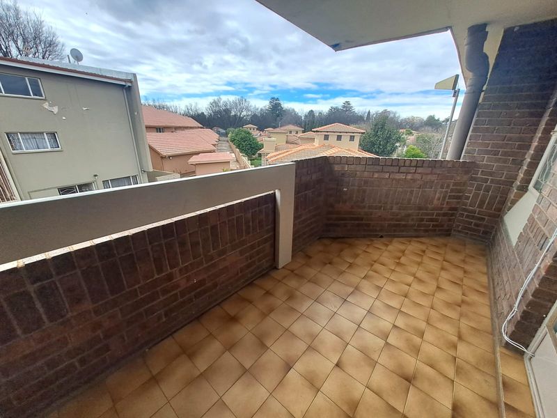 A private balcony featuring brick walling and tiled flooring, offering an elevated view of the surrounding residential complex.