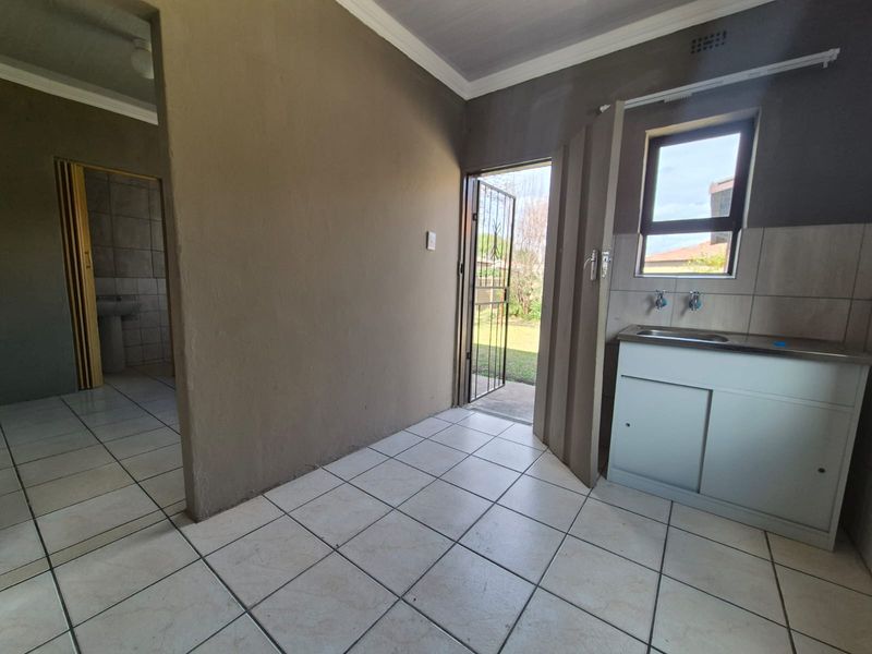 A functional scullery or utility area featuring tiled flooring, a stainless steel sink with built-in cabinetry, and direct access to the rear garden.