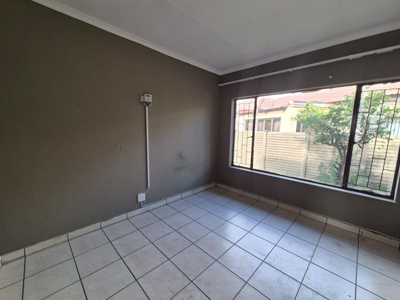 An empty bedroom featuring tiled flooring and large windows with security bars, requiring cosmetic updates to improve its overall appeal.