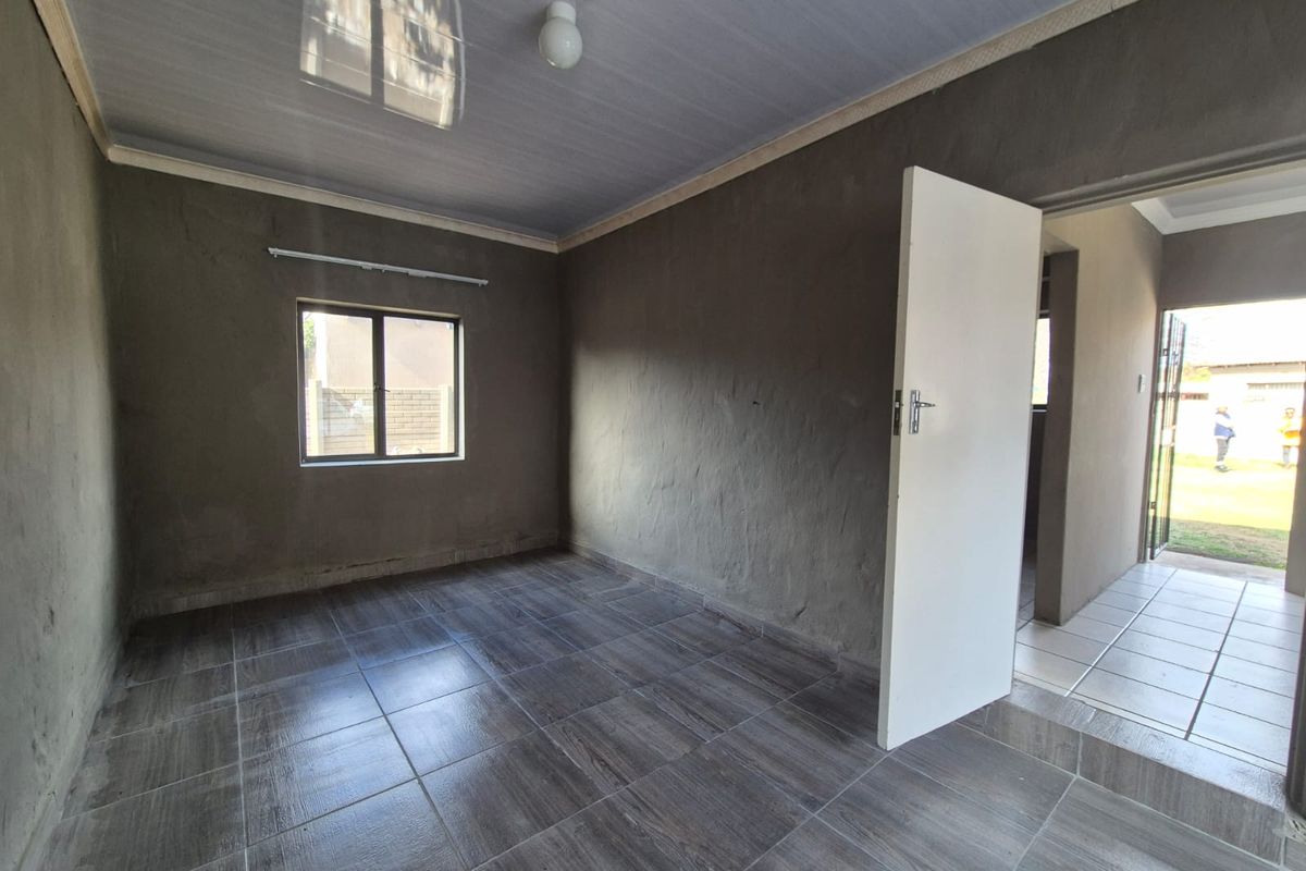An empty bedroom featuring dark tiled flooring and unfinished plastered walls, offering a blank canvas for interior design and finishing touches.