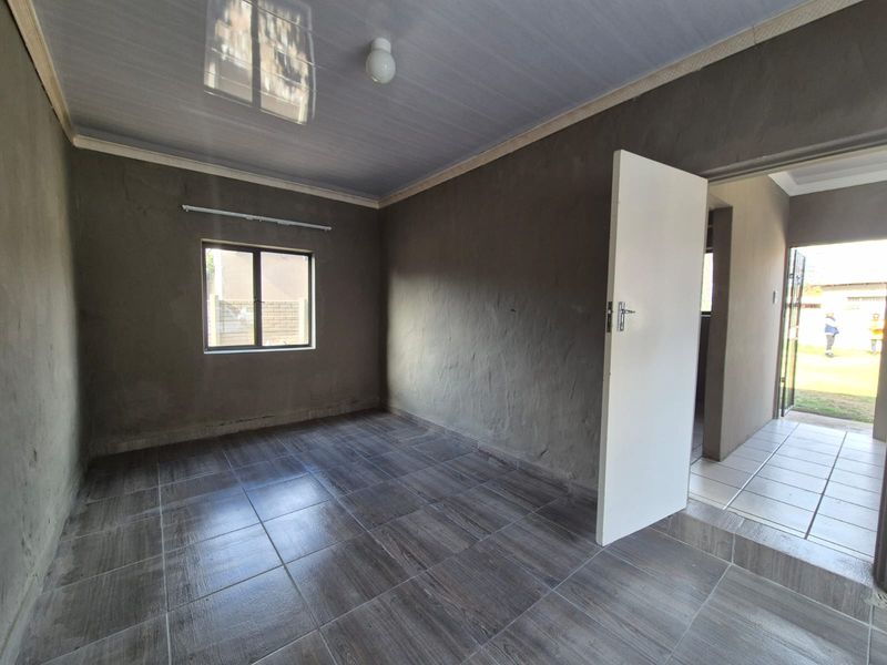 An empty bedroom featuring dark tiled flooring and unfinished plastered walls, offering a blank canvas for interior design and finishing touches.