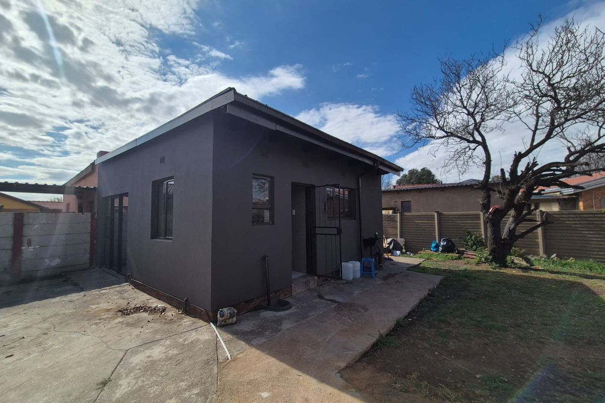 Rear view of the property featuring a dark-painted exterior, concrete driveway, and a secure entrance with a metal security gate.