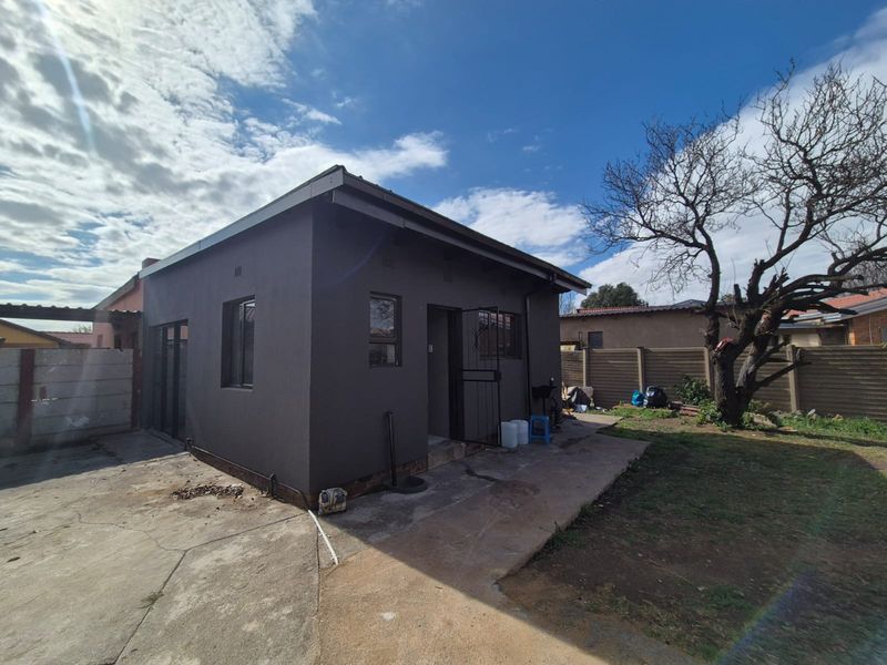 Rear view of the property featuring a dark-painted exterior, concrete driveway, and a secure entrance with a metal security gate.