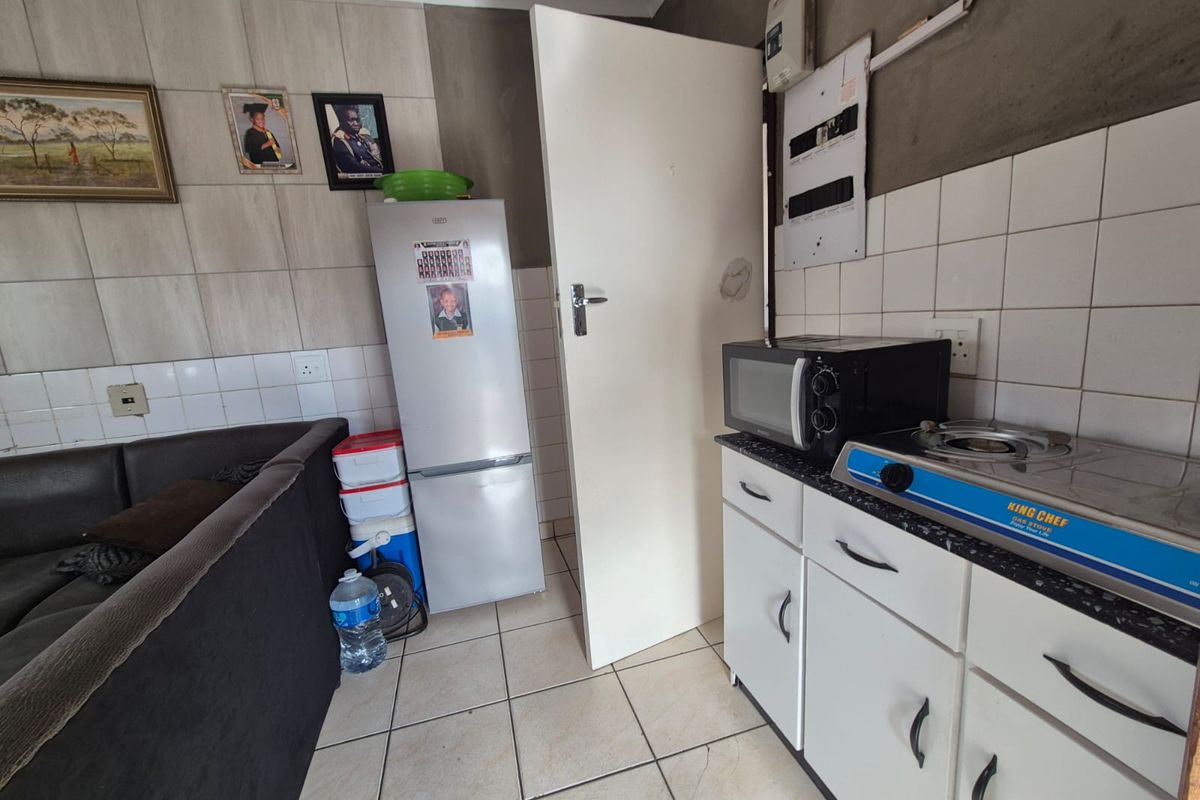 A compact kitchen area featuring tiled flooring, white cabinetry, and a tiled splashback, requiring some finishing work on the walls.