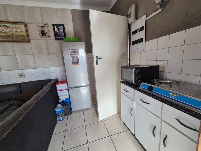 A compact kitchen area featuring tiled flooring, white cabinetry, and a tiled splashback, requiring some finishing work on the walls.