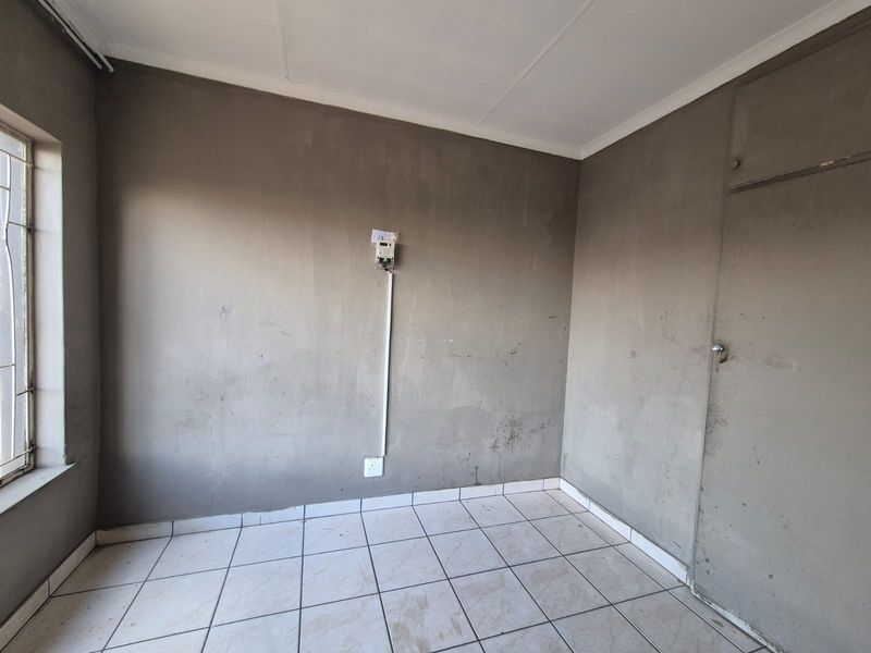 An empty bedroom featuring tiled flooring, a built-in cupboard, and unfinished plaster walls, offering a blank canvas for renovation and personalization.