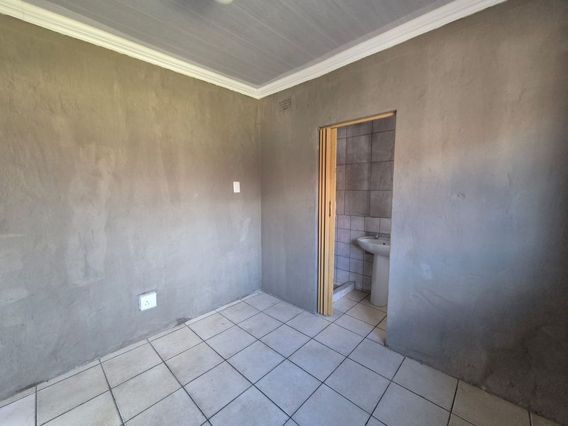 An empty bedroom featuring tiled flooring and an en-suite bathroom area with a pedestal basin, requiring finishing touches to the wall surfaces.