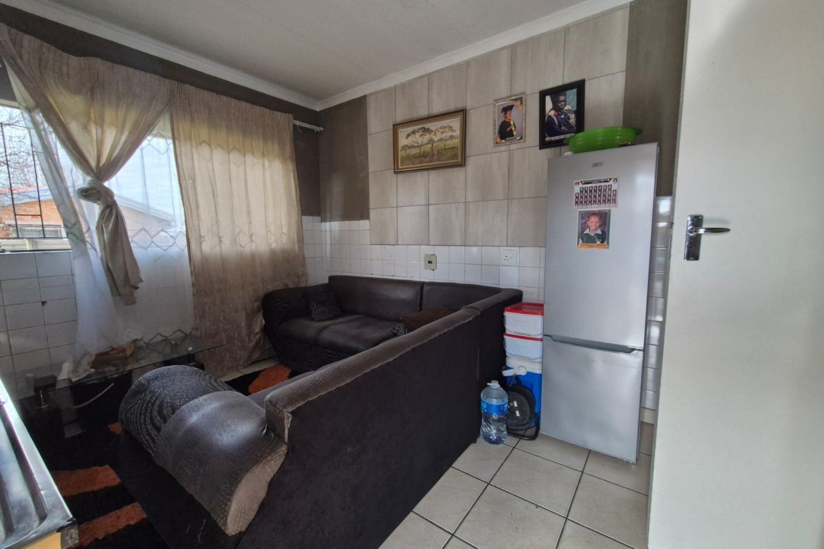 A living area featuring tiled flooring and a tiled feature wall, with security bars installed on the window.