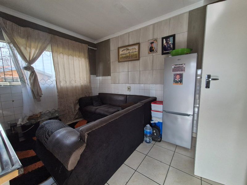 A living area featuring tiled flooring and a tiled feature wall, with security bars installed on the window.