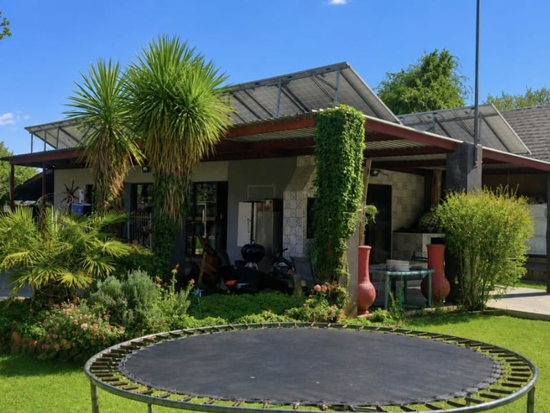 A covered outdoor patio area featuring a built-in braai and roof-mounted solar panels, overlooking a garden space.