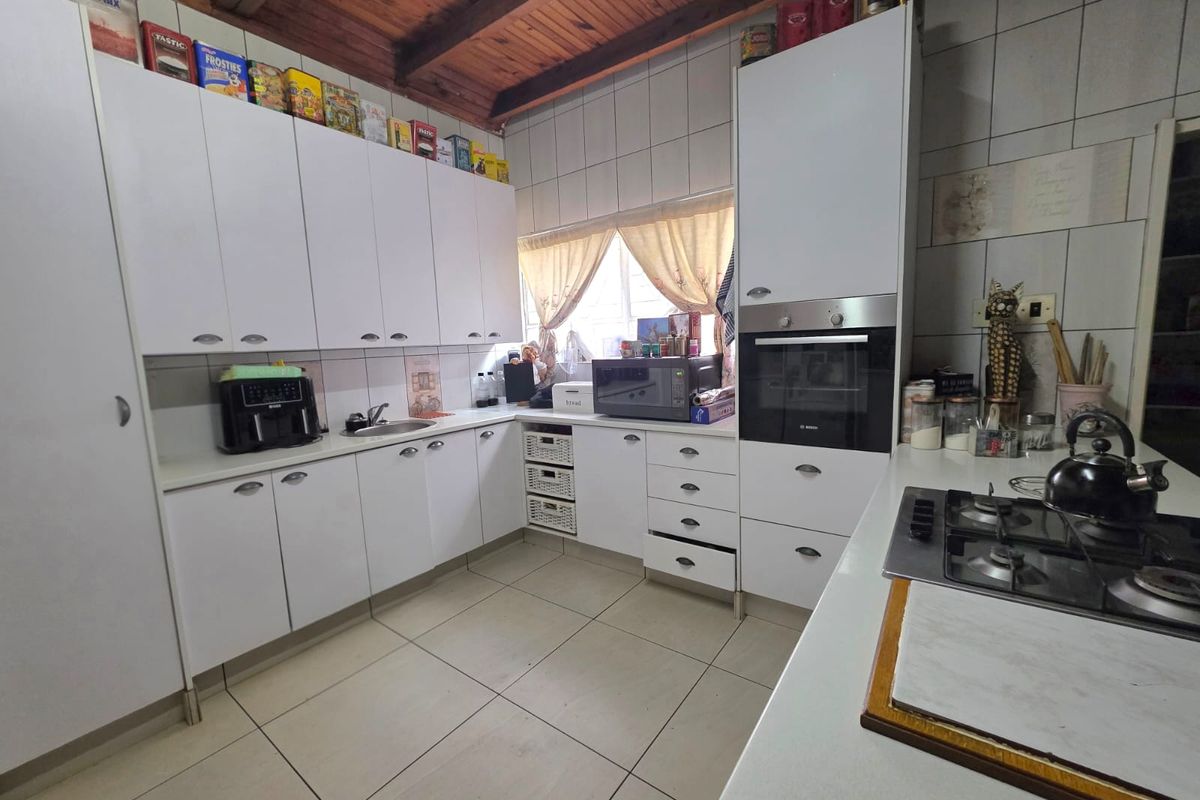 Functional kitchen featuring white built-in cabinetry, stone countertops, gas hob, built-in oven, and exposed timber ceiling beams with tiled flooring.