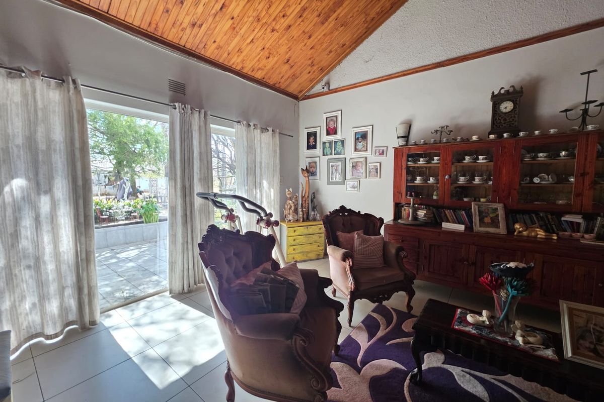 A living room featuring a vaulted timber ceiling, tiled flooring, and a sliding glass door providing access to the outdoor patio area.