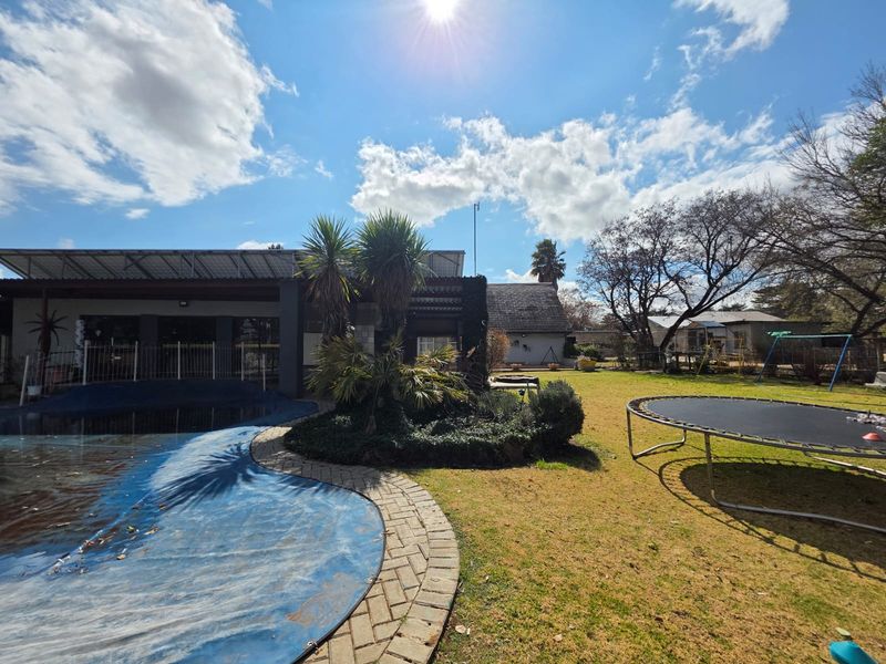 Outdoor pool area featuring a paved surround, covered patio space, and a spacious garden setting.
