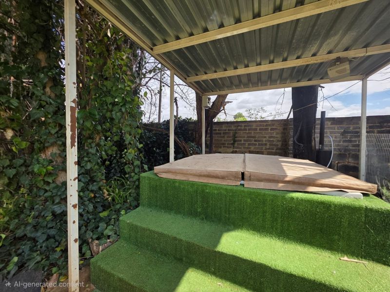 Outdoor covered patio area featuring a raised platform with artificial grass steps and a corrugated metal roof structure.