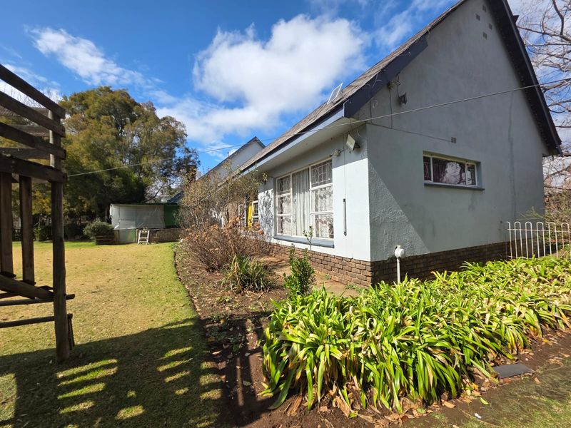 Rear view of the property showing the plastered exterior walls, brick plinth, and established garden area.