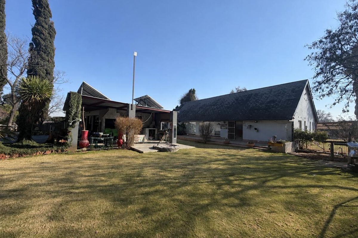 Rear view of the property featuring a large lawn, a covered patio area with a built-in braai, and solar panels installed on the roof.