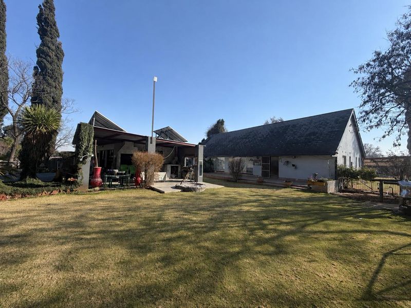 Rear view of the property featuring a large lawn, a covered patio area with a built-in braai, and solar panels installed on the roof.