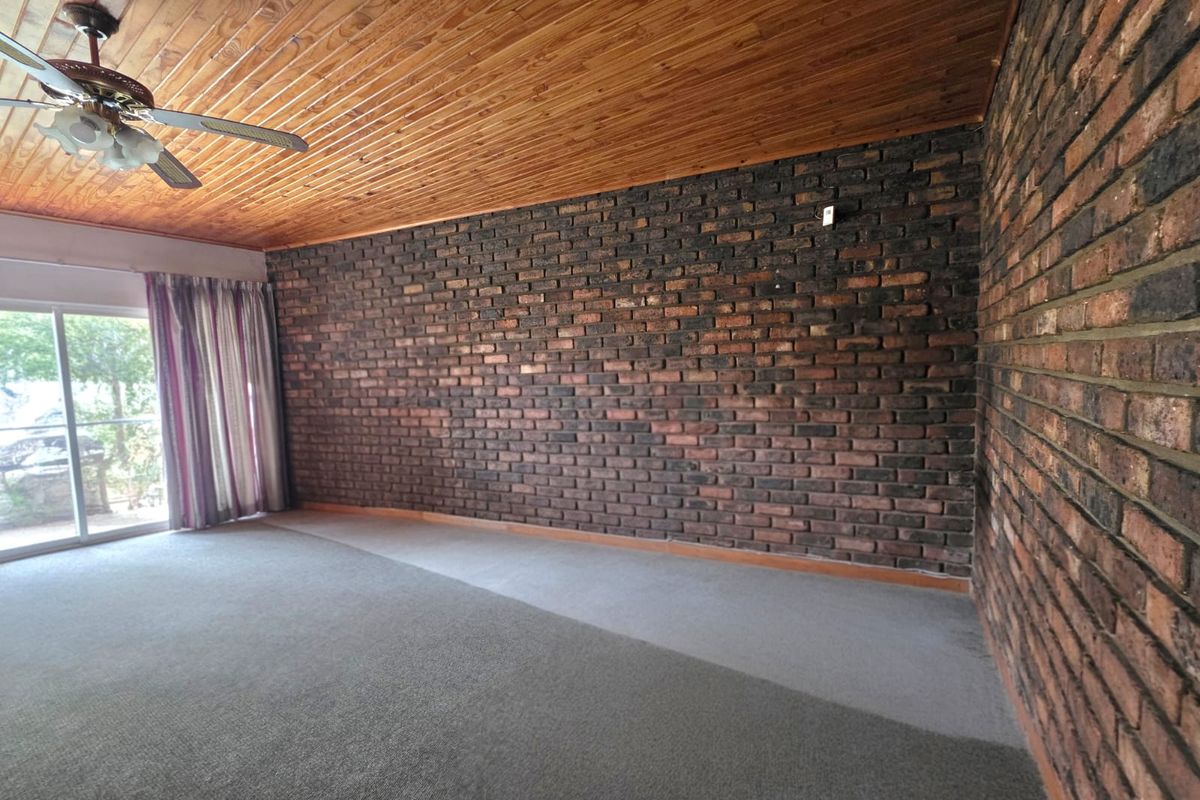 Spacious living area featuring rustic exposed brick walls, a timber-paneled ceiling with a fan, and direct access to the outdoors via a sliding glass door.