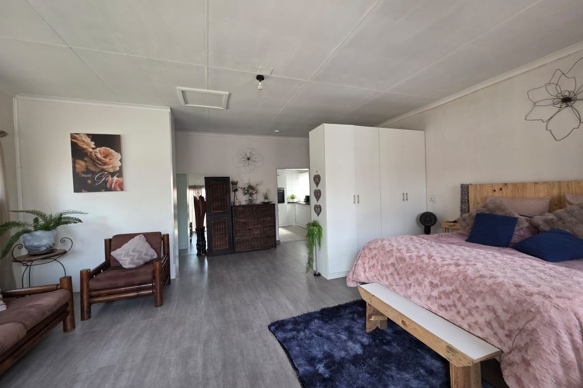 Spacious bedroom featuring built-in cupboards, laminate flooring, and neutral wall finishes, with an adjoining view into the kitchen area.