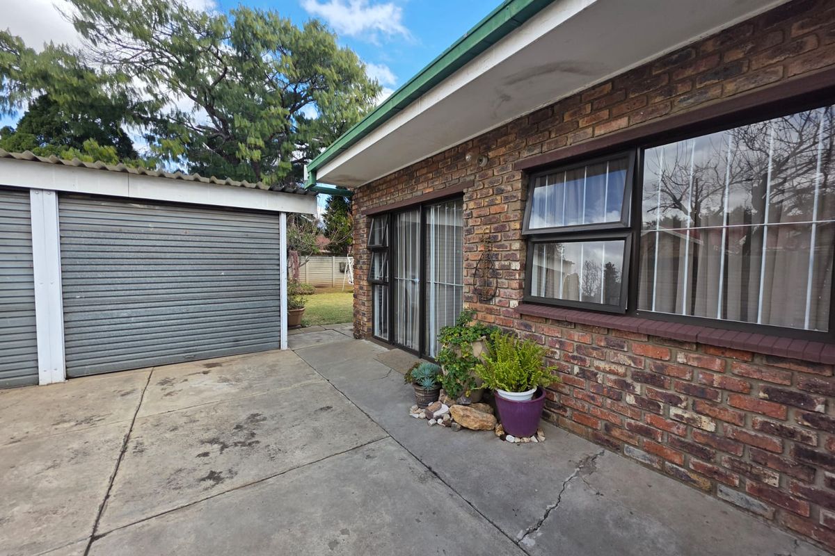 Rear exterior view of the property featuring a brick facade, concrete driveway, and a detached garage with a corrugated roof.