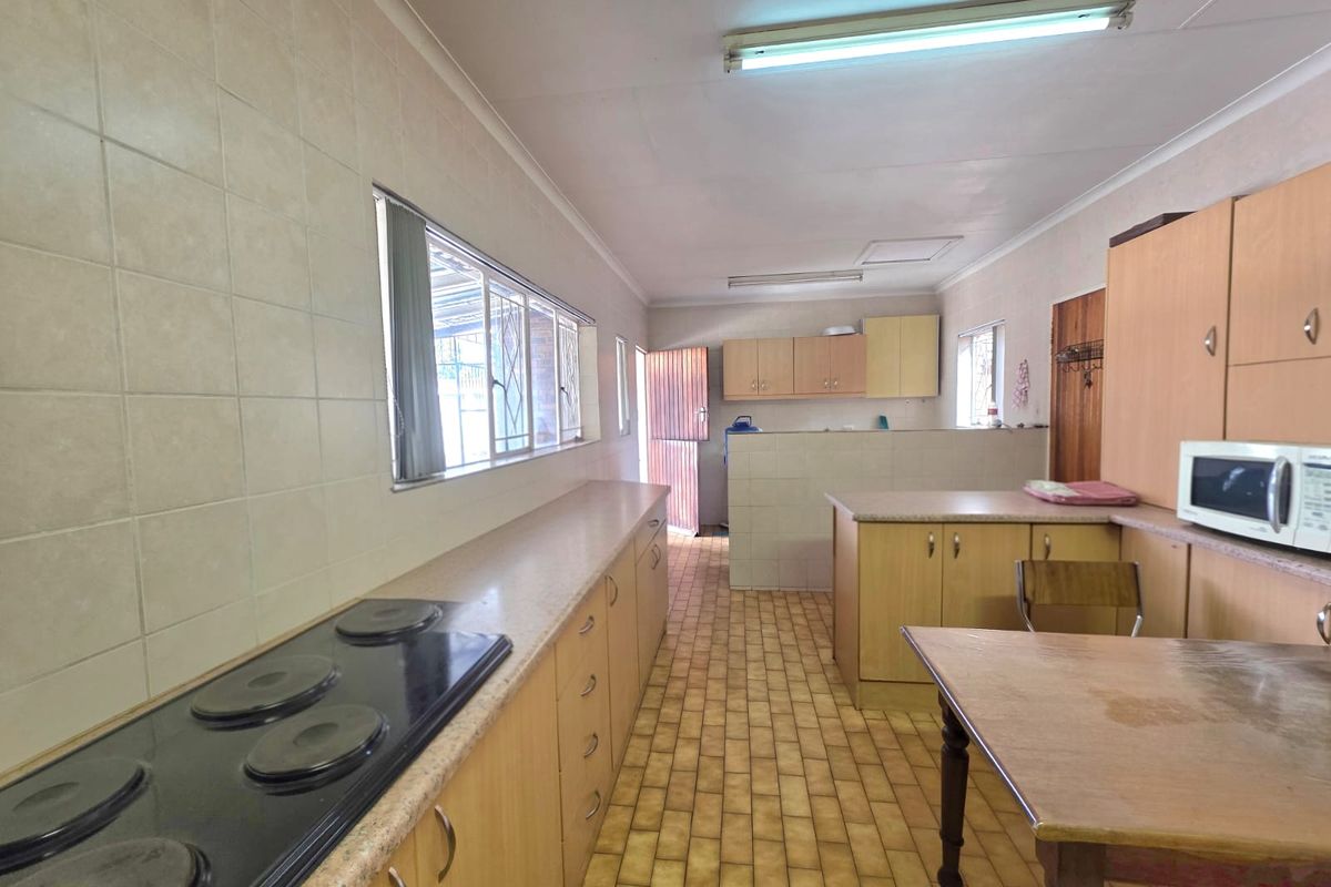 A spacious, dated kitchen featuring extensive built-in cabinetry, laminate countertops, an electric hob, and tiled flooring, offering significant potential for modernization.