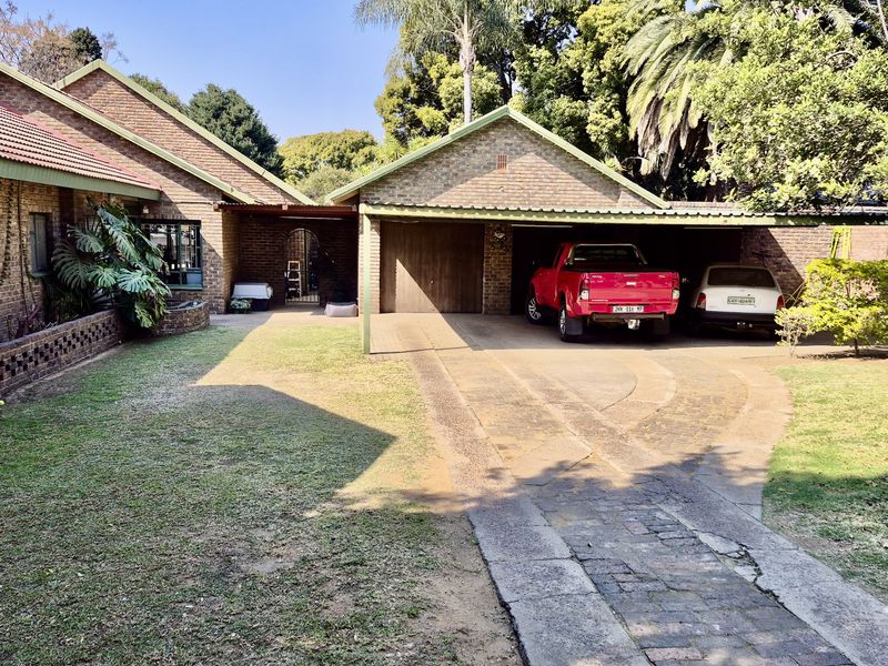 Front view of a brick house featuring a double carport, paved driveway, and established garden area.
