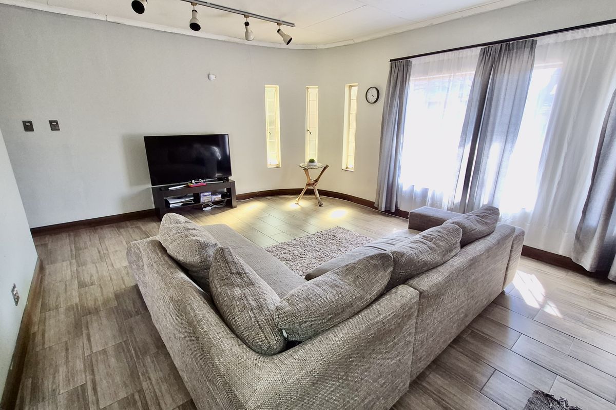 A bright living room featuring wood-look tiled flooring, track lighting, and unique vertical slit windows alongside a large window with natural light.