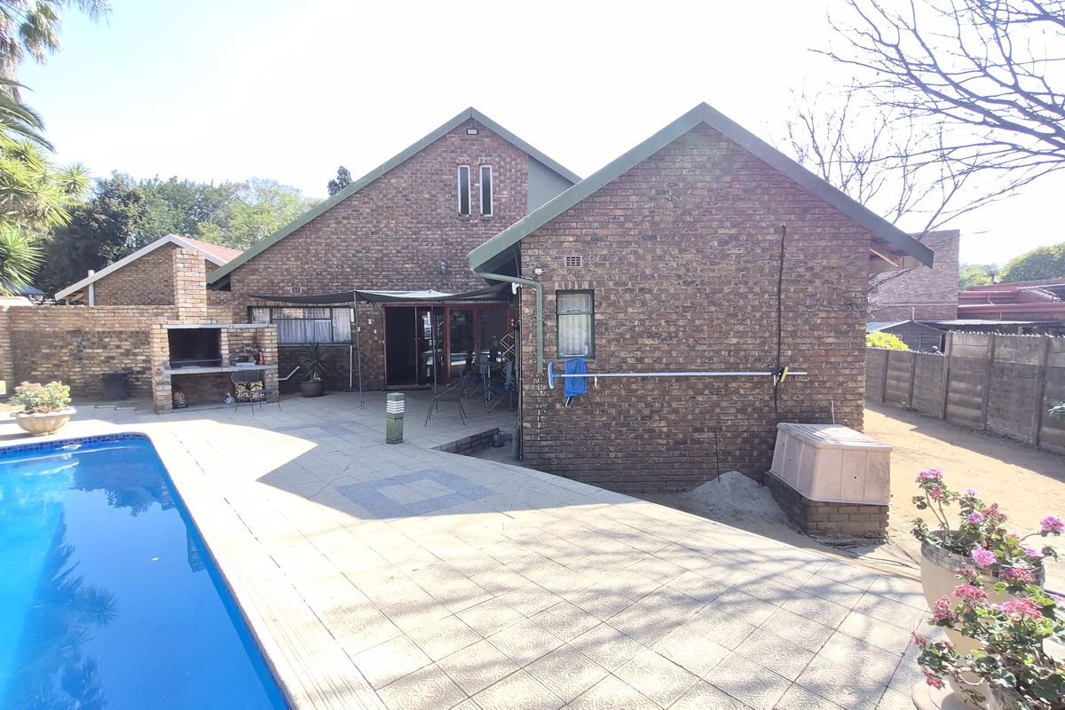Rear exterior view of the house featuring a swimming pool, paved patio area, and a built-in brick braai.
