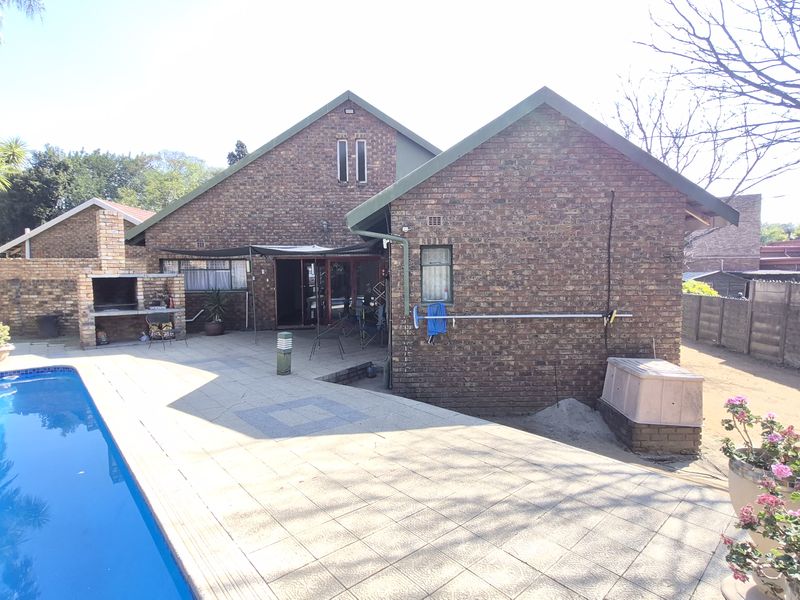 Rear exterior view of the house featuring a swimming pool, paved patio area, and a built-in brick braai.