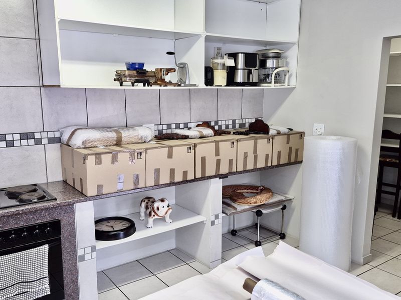 A functional scullery area featuring built-in oven, electric hob, tiled splashback, and open shelving, with an adjacent walk-in pantry space.