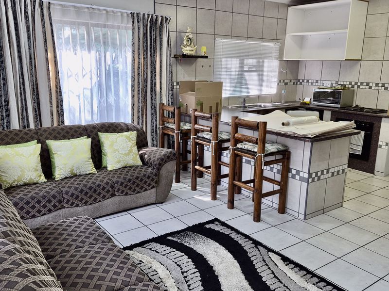 Open-plan living and kitchen area featuring tiled flooring, a central kitchen island, and built-in cabinetry with integrated cooking appliances.