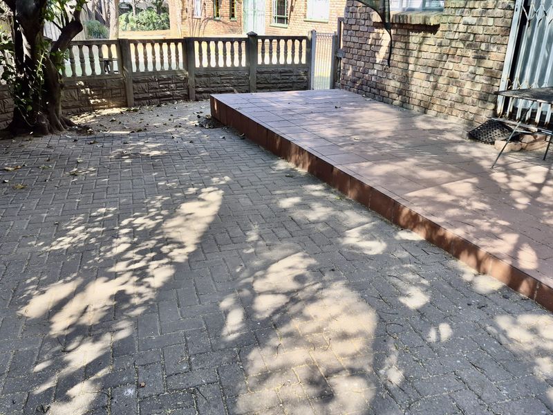 A paved outdoor patio area featuring a raised tiled platform and perimeter boundary walling, offering a functional space for outdoor living.