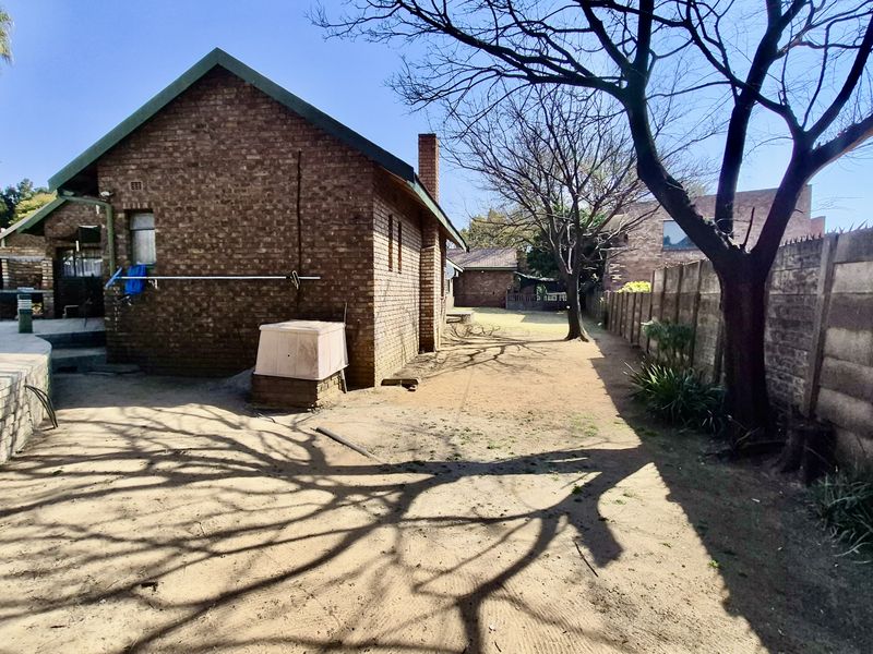 Rear view of the property featuring a brick exterior, built-in braai area, and a spacious backyard enclosed by a precast concrete wall.