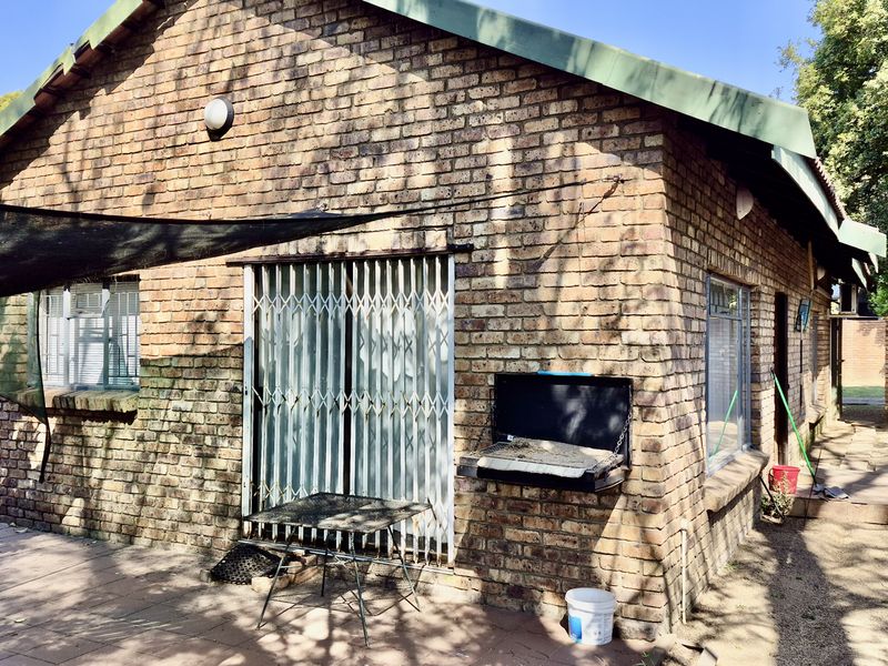 Rear exterior view of a face brick house featuring a paved patio area, security gate, and a built-in braai facility.