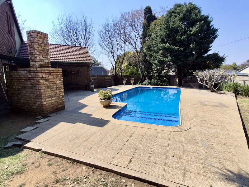 Outdoor pool area featuring a swimming pool, tiled patio, and a built-in brick fireplace, set within a private garden space.
