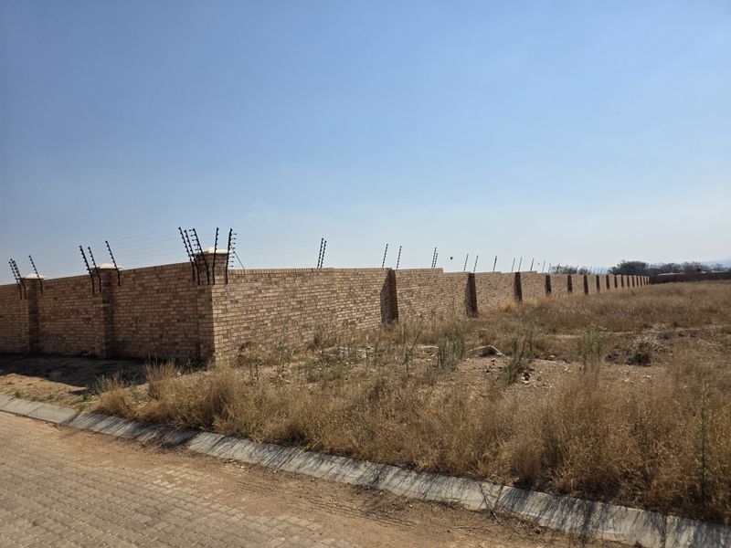 A vacant residential plot featuring a secure face brick boundary wall with installed electric fencing and a paved street curb.