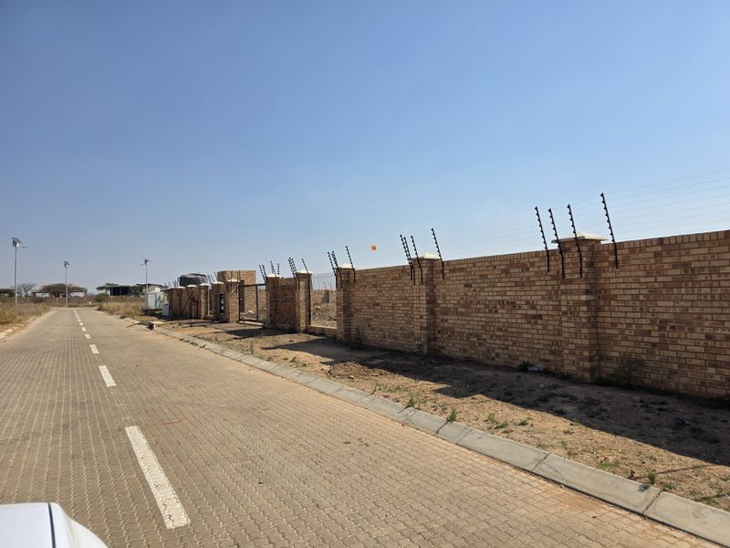 A view of a paved residential street featuring a secure brick boundary wall with installed electric fencing.