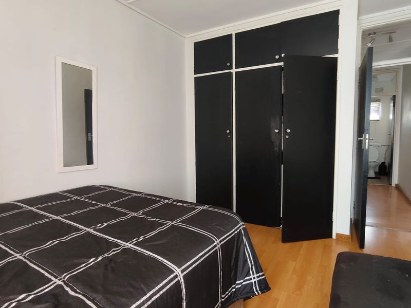 A bedroom featuring laminate flooring and a built-in wardrobe, with an adjacent view into a bathroom area.